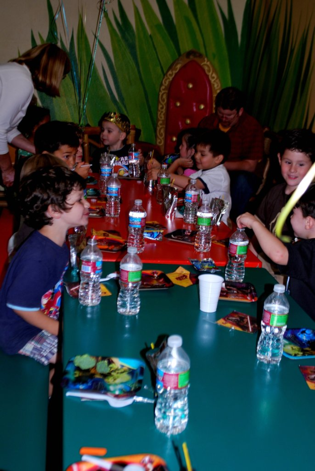 Kinder sitzen um einen Tisch mit Snacks bei einer Geburtstagsparty.