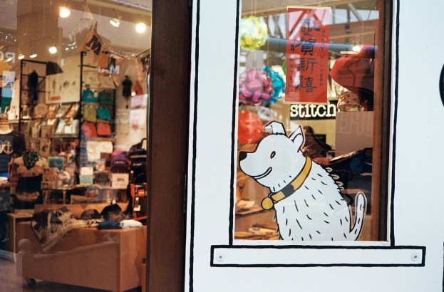 Eine Illustration eines Hundes mit Text auf der rechten Seite und links ein Raum mit Lampen, Flaggen, Regalen, Sofas, Kleidung, Dekorationen, Menschen, Stühlen und verschiedenen anderen Gegenständen.