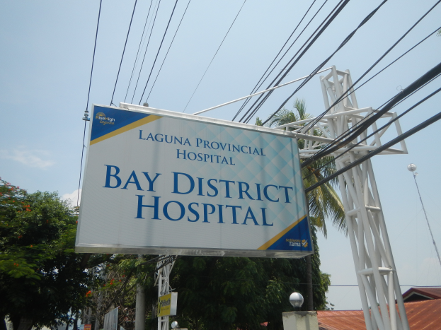 Kreis-Krankenhaus in Laguna mit einem Schild, Strommasten, Laternen, Bäumen, Gebäuden und einem bewölkten Himmel im Hintergrund.