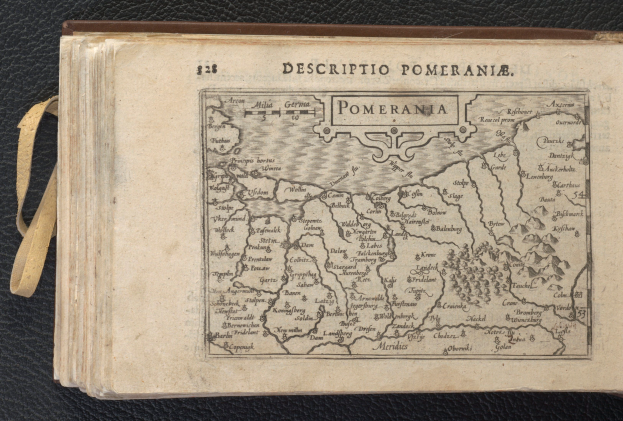 Ein altes Buch mit einer detaillierten Karte von Pommern auf einer schwarzen Oberfläche, das verschiedene Städte und Dörfer zeigt.