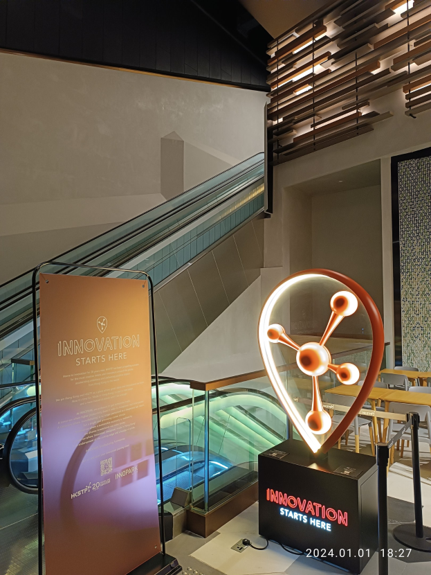 Großes Schild in einem Gebäude mit einer Rolltreppe im Hintergrund, flankiert von Tischen und Stühlen auf der rechten Seite und einer Tafel mit der Aufschrift "Innovation Starts Here" auf der linken Seite, was die Teilnahme an der HSTP20 Expo anzeigt.