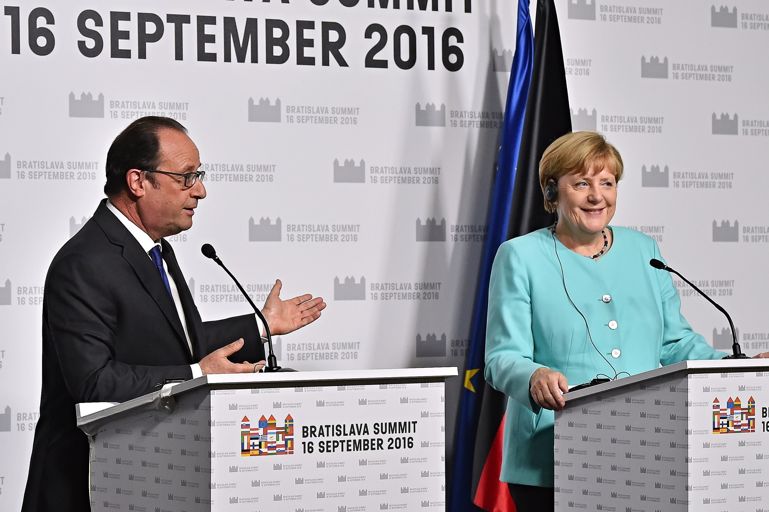 German Chancellor Angela Merkel and French President François Hollande smiling at a podium with a "Bratislava Summit 2016" banner in the background.