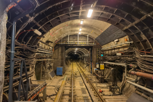 Ein Tunnel mit einer Bahnschiene, beleuchtet von Lampen oben, mit Pfählen und Drähten auf beiden Seiten und einem blauen Objekt in der Mitte, Teil der Londoner U-Bahn.