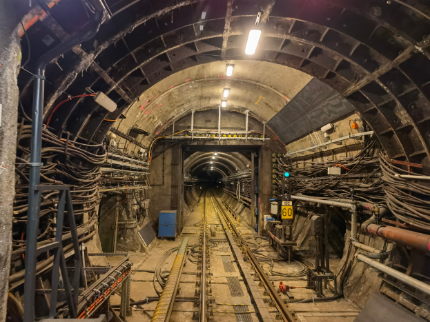 Ein Tunnel mit einer Bahnschiene, beleuchtet von Lampen oben, mit Pfählen und Drähten auf beiden Seiten und einem blauen Objekt in der Mitte, Teil der Londoner U-Bahn.
