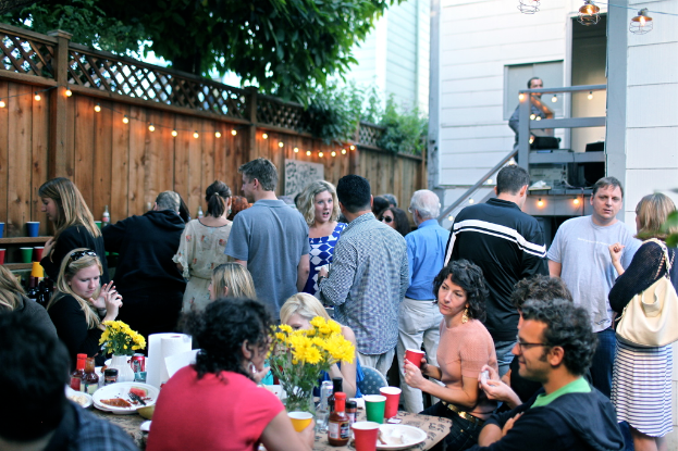 Eine Gruppe von Menschen auf einer Party, einige sitzen um einen Tisch, andere stehen.
