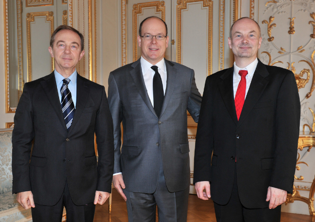 Drei Männer in Anzügen und Krawatten stehen vor einer Wand.