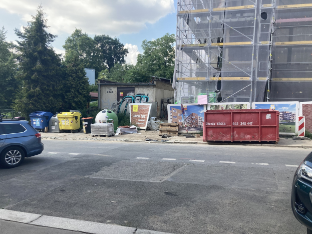 Zwei Autos neben einem Gebäude im Bau parken, mit verstreuter Schutt und Bäumen im Hintergrund.