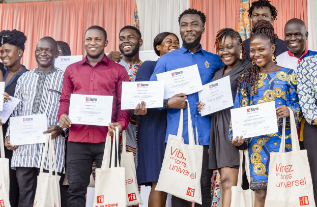 A group of smiling people holding certificates and standing with bags near curtains and a wall, indicating a celebration of an award won by the ibi bourse.