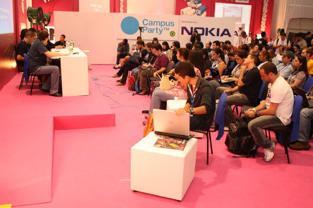 Conference with attendees seated facing a stage where speakers interact with media representatives, featuring a large hoarding in the background.