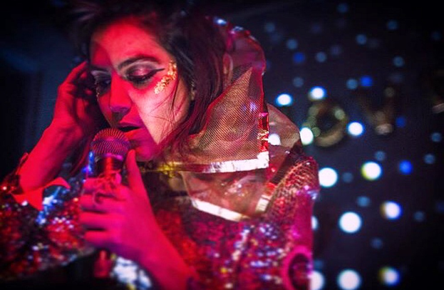 Eine Frau in einem roten Kleid singt in ein Mikrofon, beleuchtet von ein paar Lichtern im Hintergrund.