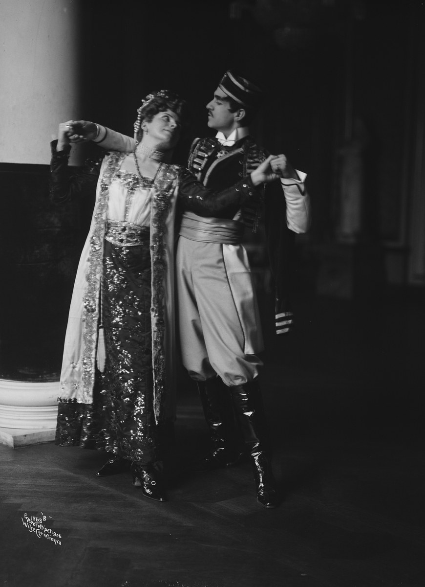 Schwarz-weiß-Foto eines Mannes und einer Frau, die in einem Ballsaal tanzen, mit einer Säule und einer Wand im Hintergrund; der Mann trägt Schuhe, was auf eine Vorstellung hindeutet.