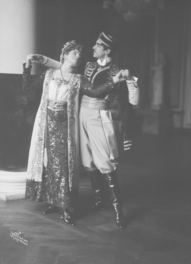 Schwarz-weiß-Foto eines Mannes und einer Frau, die in einem Ballsaal tanzen, mit einer Säule und einer Wand im Hintergrund; der Mann trägt Schuhe, was auf eine Vorstellung hindeutet.