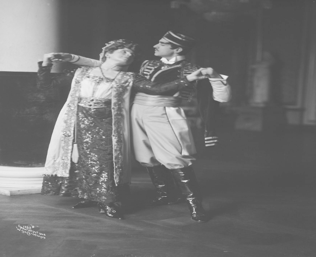 Schwarz-weiß-Foto eines Mannes und einer Frau, die in einem Ballsaal tanzen, mit einer Säule und einer Wand im Hintergrund; der Mann trägt Schuhe, was auf eine Vorstellung hindeutet.