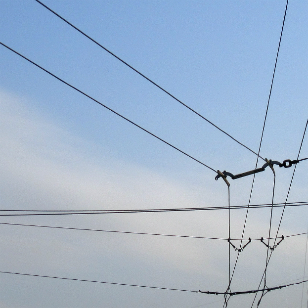 Eine Telefonleitung mit Stromleitungen im Vordergrund, ein blauer Himmel im Hintergrund und ein Gebäude unten im Bild.