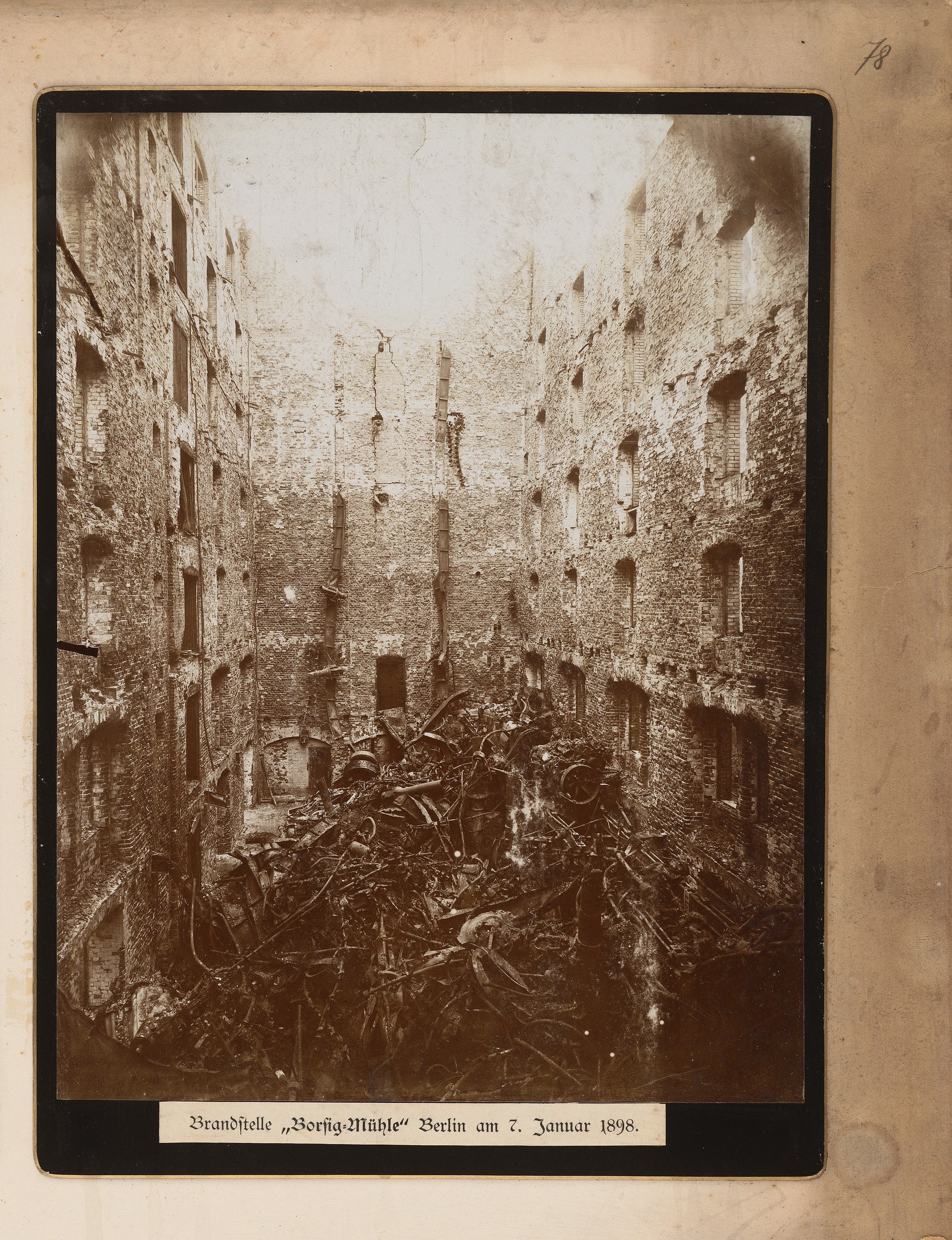 Ein Schwarz-Weiß-Foto eines stark beschädigten Stadtgebäudes, das von einem Photo-Rahmen umgeben ist, mit verstreuter Trömmern und zerbrochenen Fenstern und fadenscheinigem Text unten.