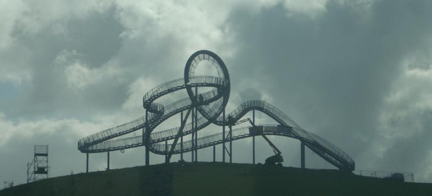 Eine Achterbahn auf dem Höhepunkt eines Hügels unter einem bewölkten Himmel, mit Stützpfählen und -strukturen.