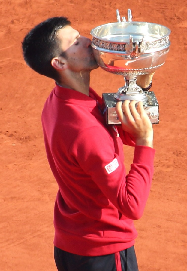 Novak Djokovic hält den French-Open-Pokal nach seinem Sieg gegen Rafael Nadal im Endspiel der Herren-Einzel, küssend den Pokal mit einem triumphierenden Ausdruck.