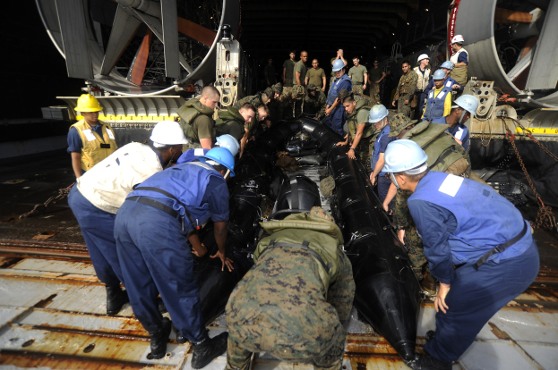 Gruppe von Männern in Helmen und Uniformen, die an einem U-Boot in einem Schiffbauwerk arbeiten.