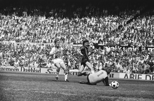 Schwarzes Foto von Männern, die Fußball auf einem Feld mit Zuschauern im Hintergrund und einem Banner mit der Aufschrift "Bundesliga 1978-79 Ajax 1-1 Hannover 96" spielen.