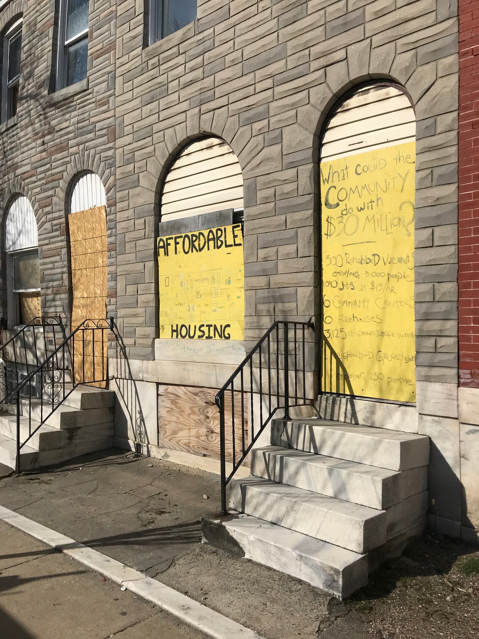 Ein verbarrikadiertes Gebäude mit einer Tafel, die "Bezahlbarer Wohnraum" lautet, eine Treppe mit Geländern, die darauf führt, und eine Straße unten.