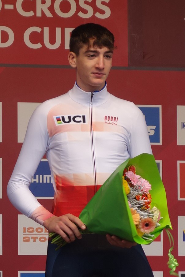A man stands on a podium holding a bouquet of flowers, celebrating with a confident and proud posture.
