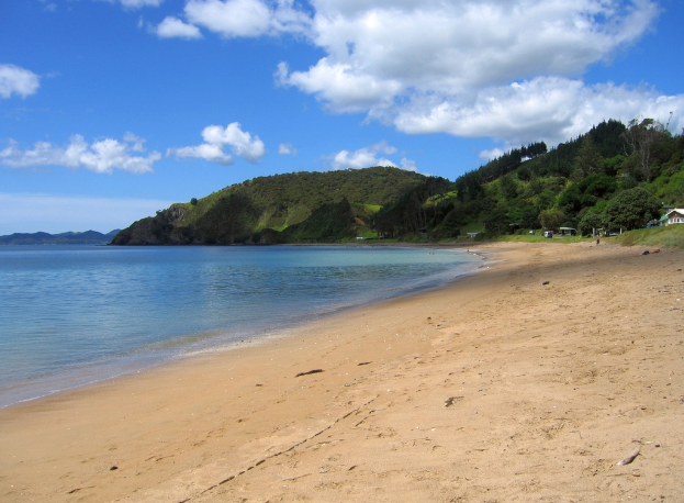 Eine Seelandschaft mit einem Meer auf der linken Seite, Hügel in der Mitte, einem Himmel oben, Schuppen auf der rechten Seite und einem Strand unten.