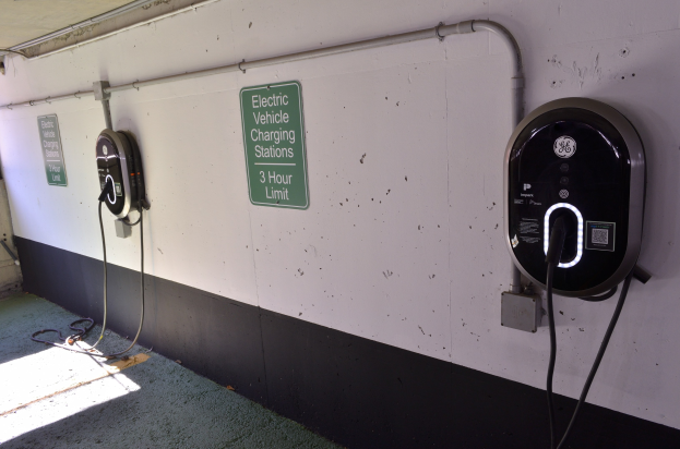 Ladestationen für Elektrofahrzeuge an einer Wand in einer Tiefgarage montiert, mit Informationsschildern darüber und dem Garagenboden darunter sichtbar.