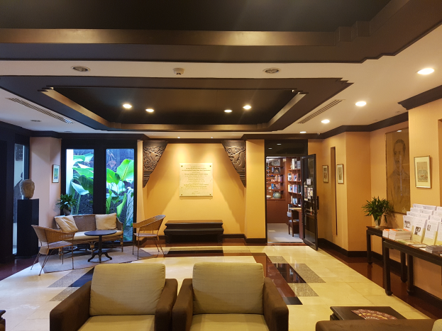 Ein Hotel-Foyer mit Sofas, St├╝hlen, Tischen, Topfpflanzen, B├╝chern in Regalen, Deckenleuchten, Wandschmuck und Dekoration auf Beistelltischen, geflutet mit nat├╝rlichem Licht von Fenstern und T├╝ren.