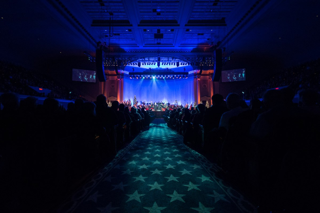 Ein großer Auditorium mit Sitzplätzen, einer Bühne mit Musikern und Überkopfbeleuchtung und Fernsehern, was auf einen Konzertsaal während der Nationalkonvention 2019 hinweist.