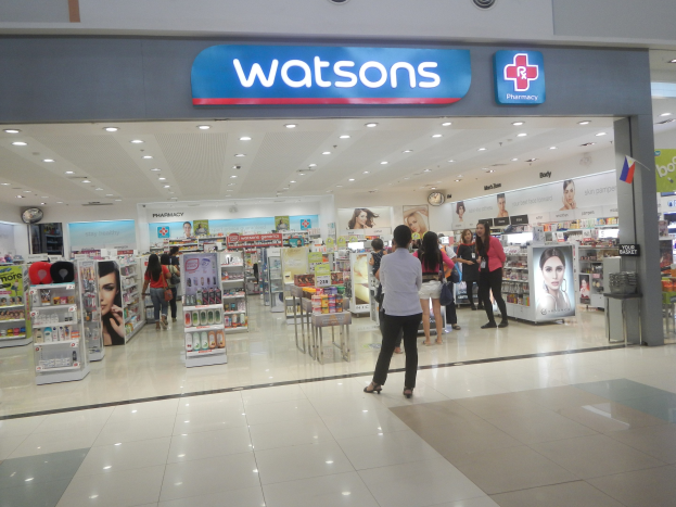 Watsons Apotheke im Einkaufszentrum mit Menschen, Regalen, Schildern, einer Wanduhr und Deckenlampen.