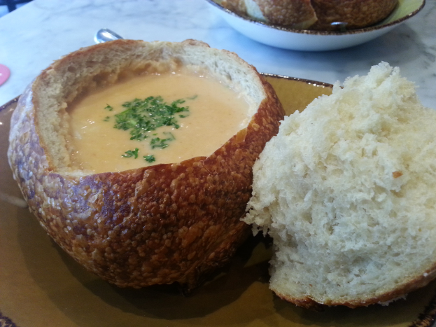 Ein Teller mit Clam Chowder im Vordergrund und eine Schüssel mit Broten im Hintergrund.