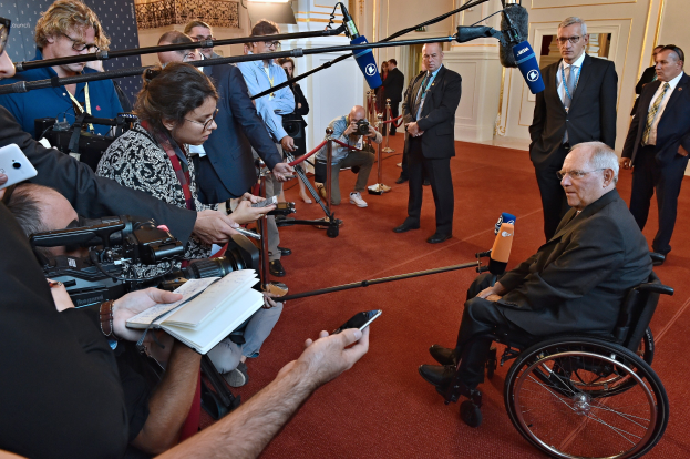 Ein Mann im Rollstuhl wird von Reportern mit Kameras, Handys und Mikrofonen mit Ständern umgeben.