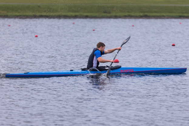 Eine Person in einem Kajak auf dem Wasser, die ein Paddel hält, mit Gras im Hintergrund und einigen Gegenständen im Wasser.