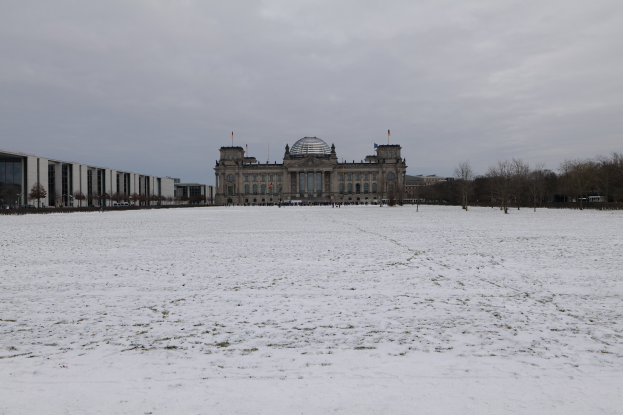 Das Reichstagsgebäude in Berlin, Deutschland, mit Schnee bedeckt, umgeben von Bäumen und Polen, mit dem Himmel im Hintergrund.