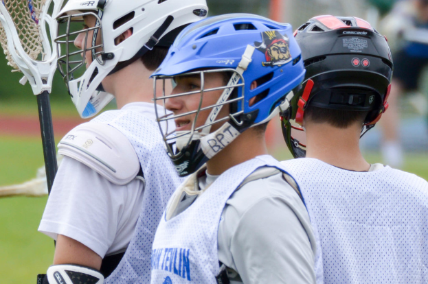 Zwei Männer spielen Tischtennis drinnen, mit mehreren Zuschauern, die stehen und sitzen, einigen leeren Stühlen und sichtbaren Werbetafeln, mit Text in der linken unteren Ecke.