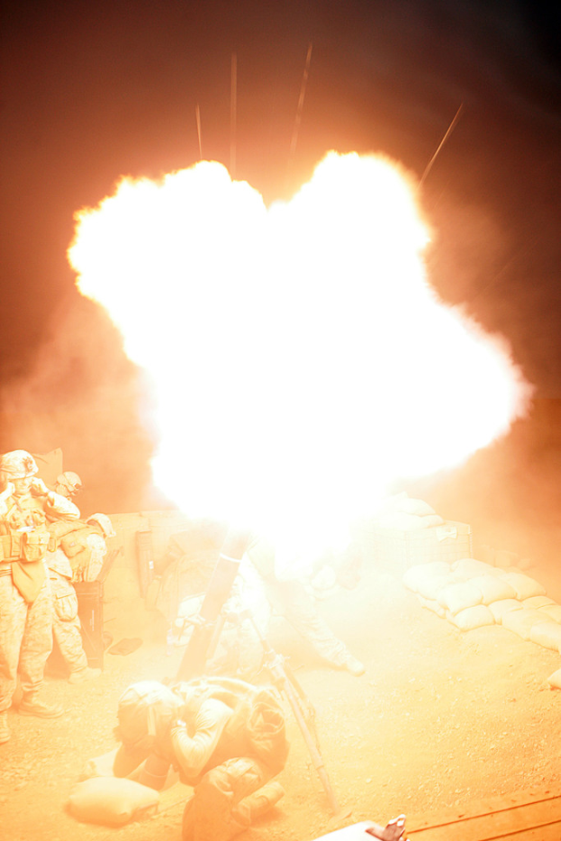 Mehrere Personen in Uniform und Helmen auf einem Gelände mit Taschen, mit einem Feuer in der Mitte der Szene.