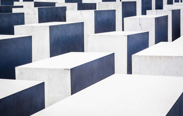Aerial view of the Holocaust Memorial to the Murdered Jews of Europe in Berlin, featuring numerous white and blue concrete slabs arranged in a grid pattern.