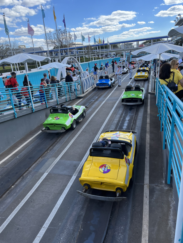 Eine Gruppe von Menschen, die auf einer Achterbahn im Disney's Hollywood Studios fahren, umgeben von Geländern und Fahnen, mit Bäumen und Gebäuden im Hintergrund unter einem bewölkten Himmel.