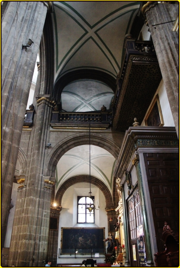 Ein prunkvoller Innenraum eines Palastes mit Schränken, beleuchteten Säulen, Wandskulpturen, einem großen Rahmenbild und einer Deckenleuchte.