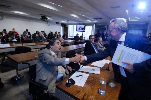 Eine Gruppe von Menschen ist in ein Gespräch vertieft, mit einigen anderen im Hintergrund unter einer Decke mit Beleuchtungskörpern, wie auf einem Fernsehbildschirm zu sehen.