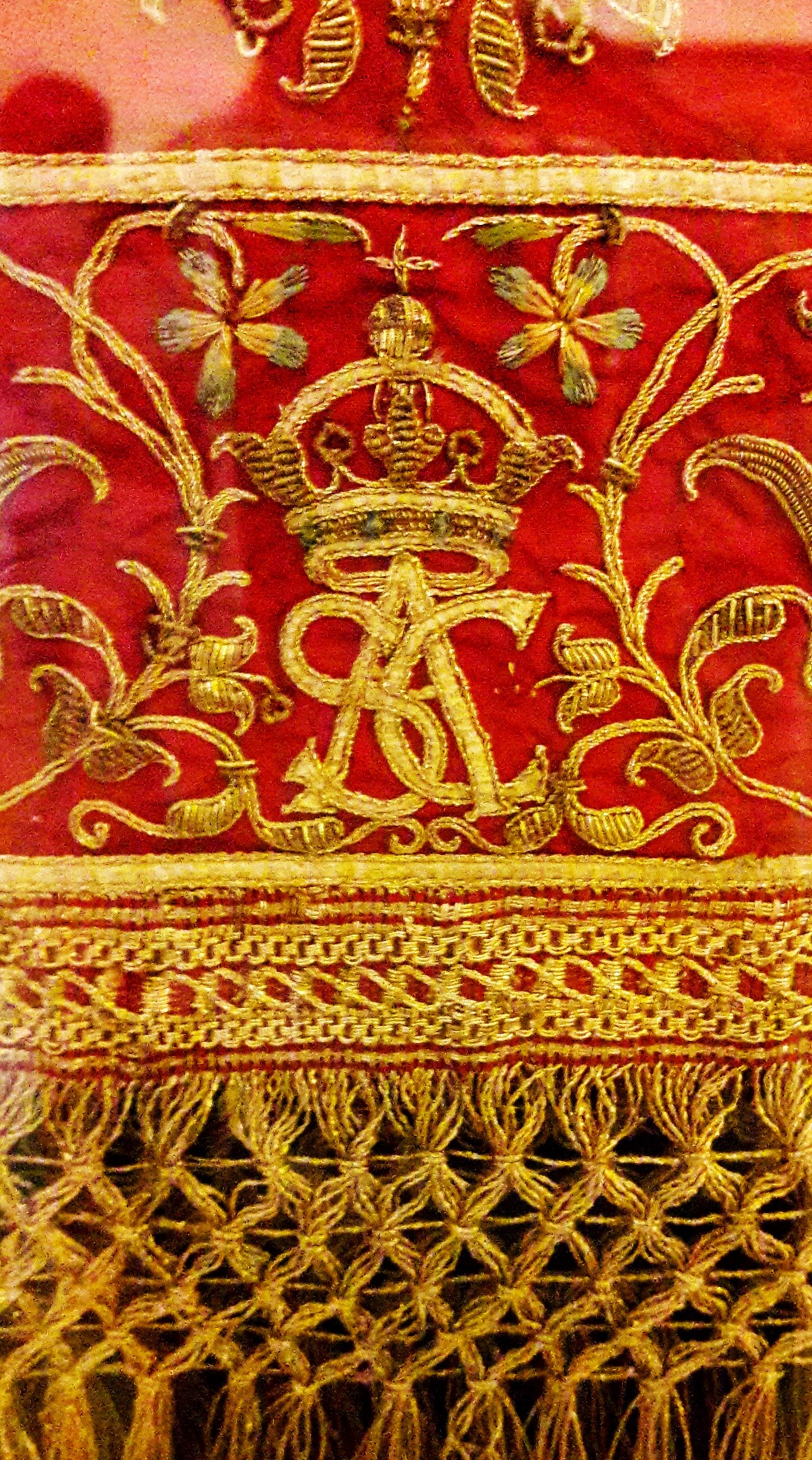 Nahaufnahme eines roten und goldenen Tuchs mit einer Krone und aufwändiger Goldstickerei, das einen luxuriösen Eindruck vermittelt.