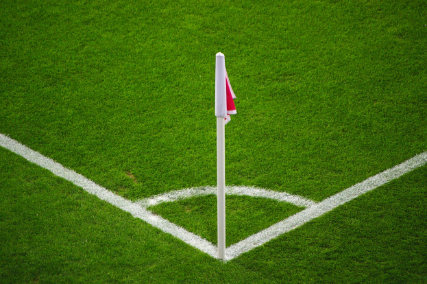 Ein Fußballfeld mit grünem Rasen, weißen Begrenzungslinien und einem Elfmeterpunkt, der durch einen weißen Pfosten mit einer roten und weißen Flagge markiert ist.
