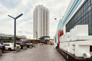 A bustling central market in Kuala Lumpur, Malaysia, featuring tall buildings, street poles, street lights, motor vehicles, pedestrians on the footpath, name boards, trees, and a cloudy sky.