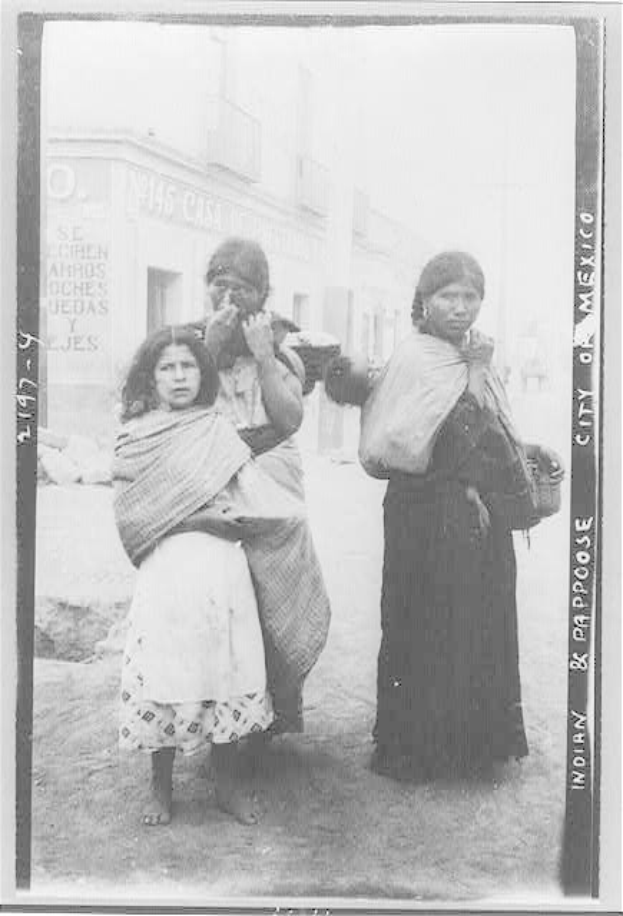 Drei Frauen, die zusammen auf einer Straße in Mexiko-Stadt stehen, mit Gebäuden im Hintergrund, auf einem Schwarz-Weiß-Foto.