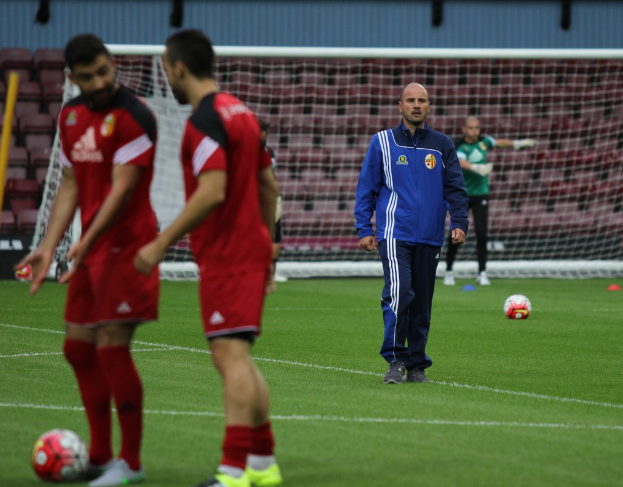 Ein Fußballfeld mit Spielern darauf, zwei Bälle sind sichtbar und ein leerer Stadion im Hintergrund.
