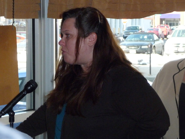 Eine Frau spricht mit einer anderen Person hinter sich, mit einem Fenster, das viele Fahrzeuge zeigt.